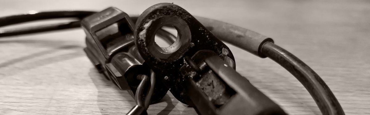 An ABS wheel speed sensor taken off a car, lying on a wooden table with its cable and plug