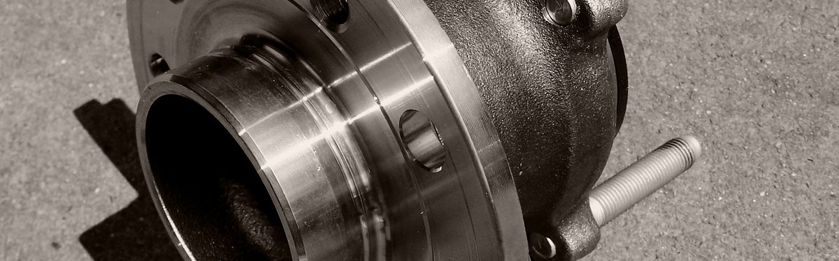 A wheel hub bearing assembly on pavement: the round steel flange, its center spigot and the cast bearing housing