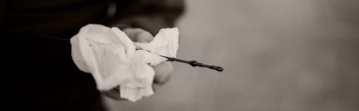 A hand holding an oil dipstick drawn from an engine