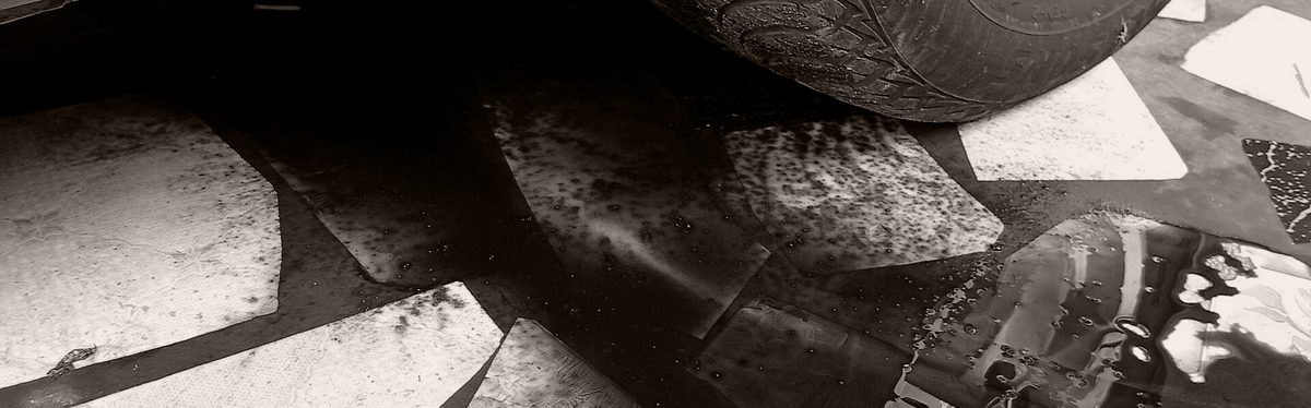 A dark fluid stain spreading across the ground beside a parked car's tire