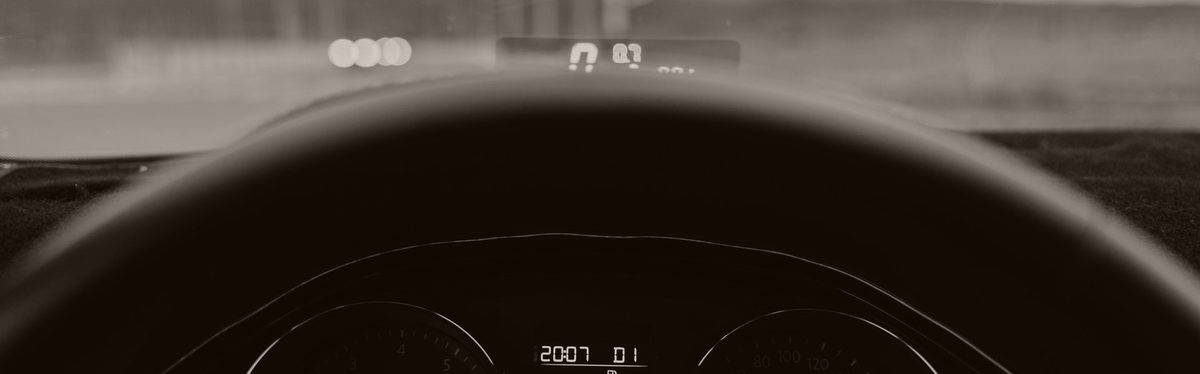 The driver's view over a steering wheel onto a lit tachometer and speedometer, the car in Drive on an open road