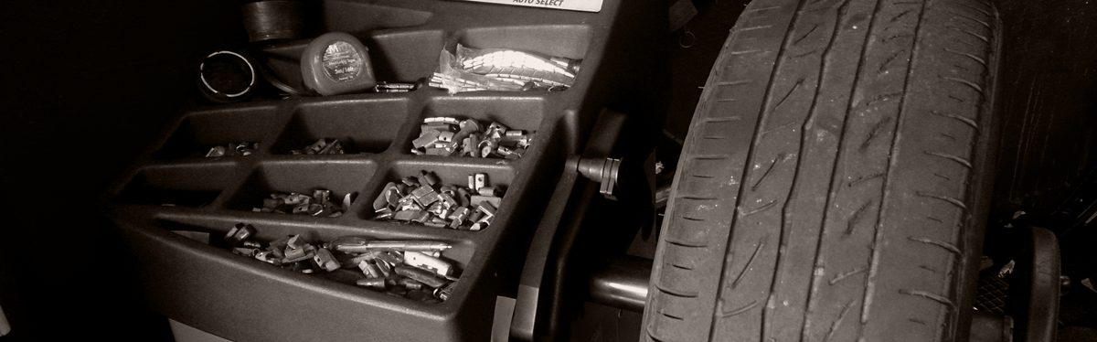 A wheel balancing machine in black and white, its tray full of small wheel weights beside a tire on the spindle.