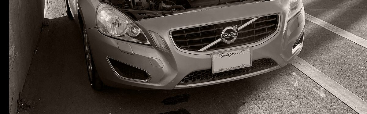 A silver sedan pulled over at the roadside with its hood raised and fluid spots on the pavement below