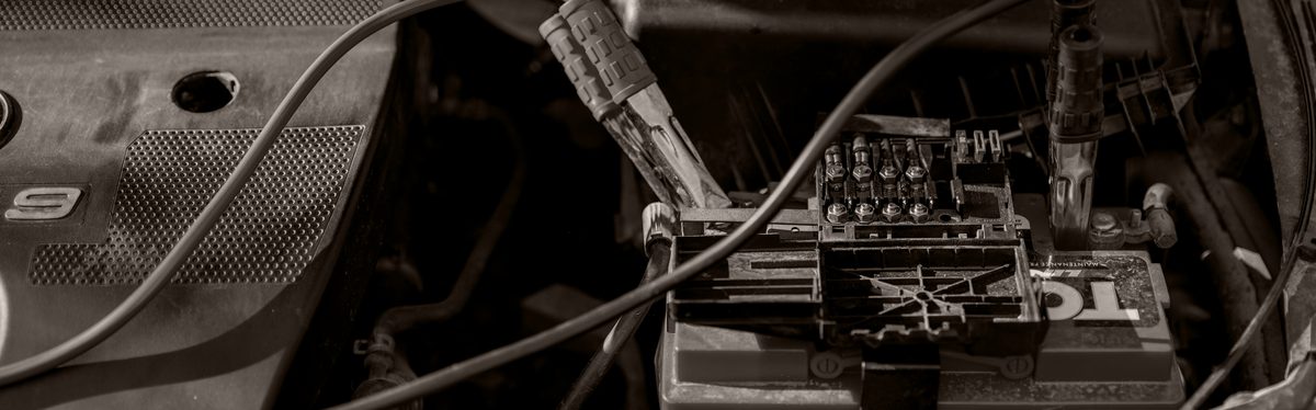 Red and black jumper cable clamps attached to the terminals of a car battery under the hood