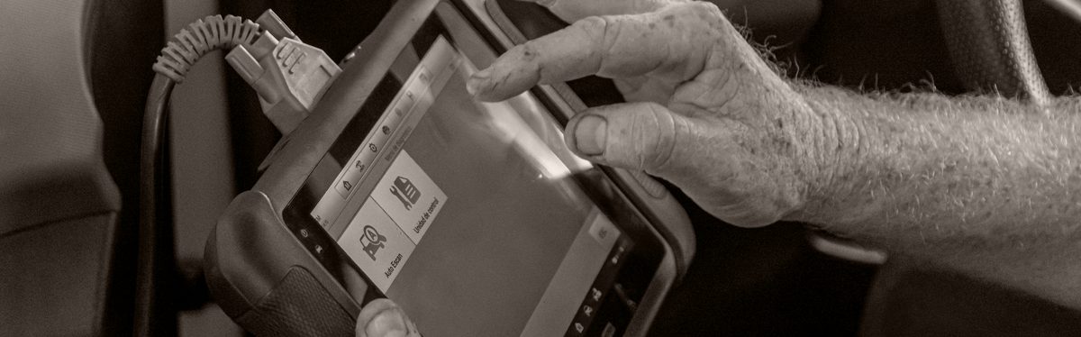 A technician holding a scan tool beside the steering column