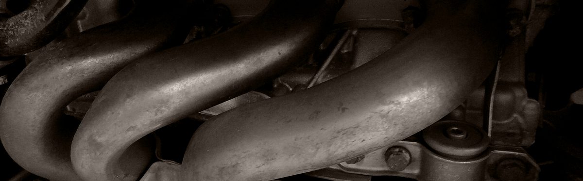 An exhaust manifold bolted to the side of an engine, its metal discolored from heat.