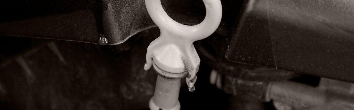 An oil dipstick with a white loop handle standing in an engine