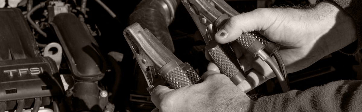 A pair of hands holding two jumper cable clamps over the open engine bay of a car