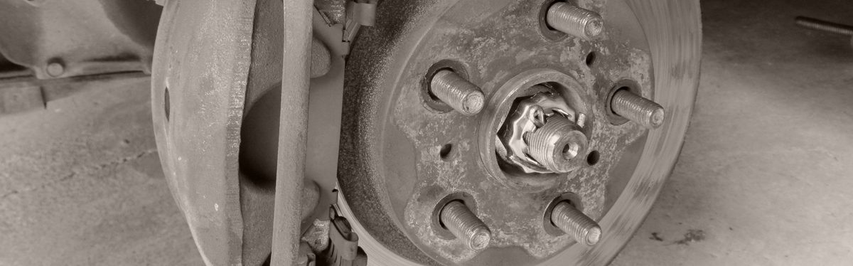 A front disc brake with the wheel off: the caliper and its bracket on a rusty, ridged brake rotor