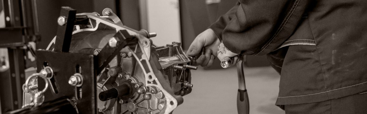 A technician turning a wrench on an automatic transmission mounted on a bench stand in a workshop
