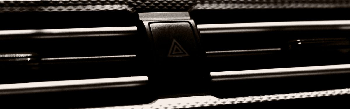 A red hazard warning triangle on its button, on a dark dashboard between two air vents