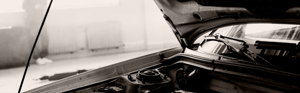 A raised hood over an engine bay in a workshop, seen from the wing, with the strut tower and windshield cowl in frame