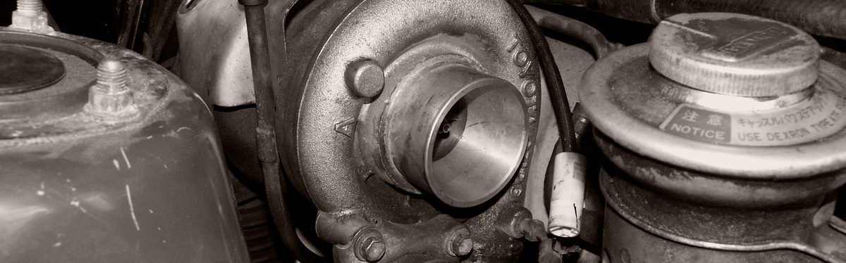 A turbocharger bolted into an engine bay, its snail-shaped compressor housing and round air inlet facing the camera