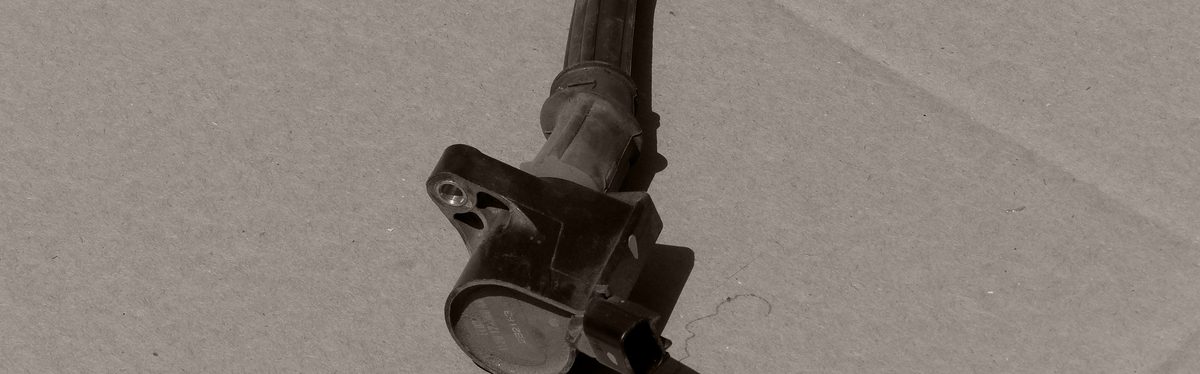 A coil-on-plug ignition coil taken out of the engine, lying on cardboard beside the bolt that holds it down
