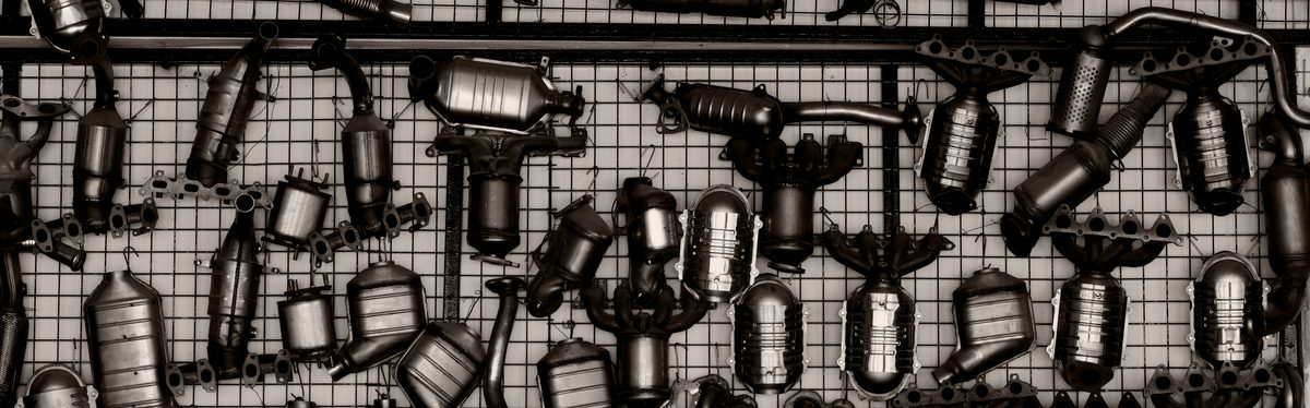 A workshop wall hung with dozens of used catalytic converters and exhaust manifolds on a wire mesh panel
