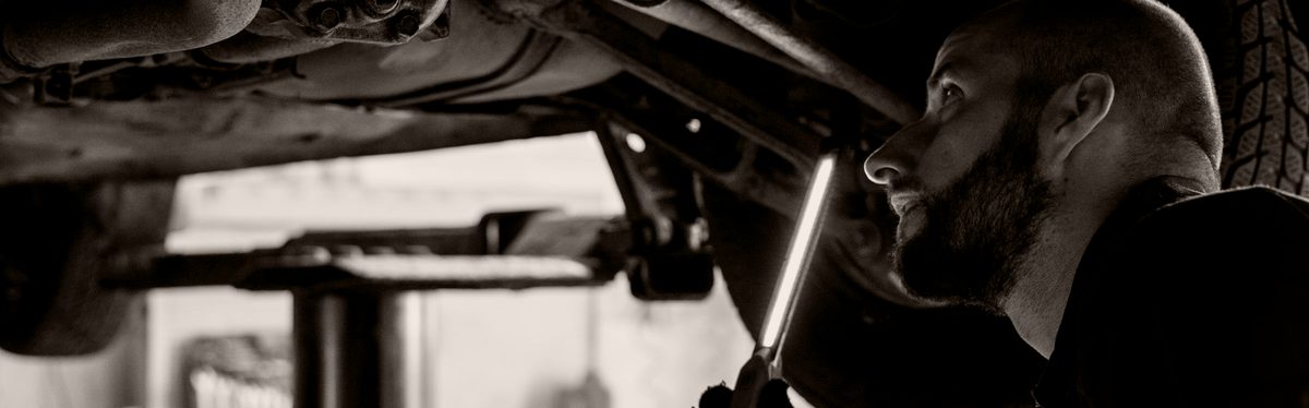 A mechanic under a raised car with an inspection light