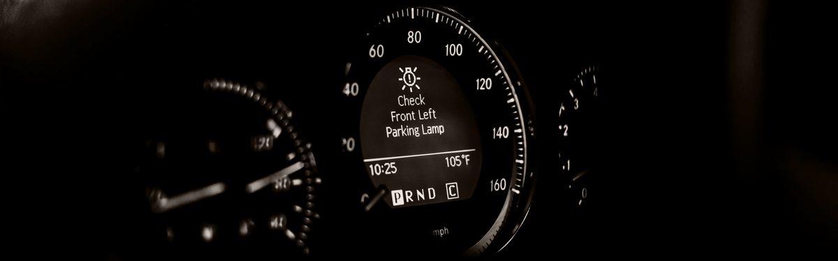 A car's speedometer in black and white, with a text warning message on the screen at its center