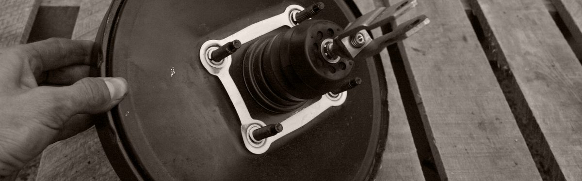 A vacuum brake booster off the car, held by hand, its pushrod and mounting studs facing the camera