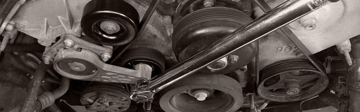 A serpentine belt around an engine's alternator and pulleys, a wrench on the spring-loaded idler taking the tension off