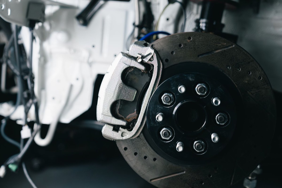 Car brake caliper and rotor with the wheel removed, brake pads visible inside the caliper