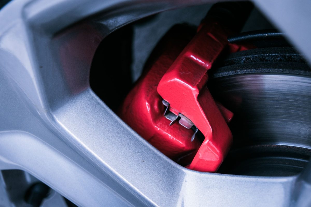 A red brake caliper seen through alloy wheel spokes, with the rotor edge and pad backing beside it