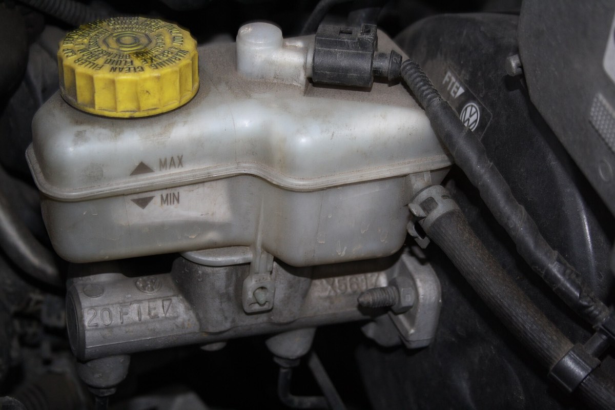 A brake fluid reservoir on a master cylinder, showing MAX and MIN level marks and a yellow warning cap
