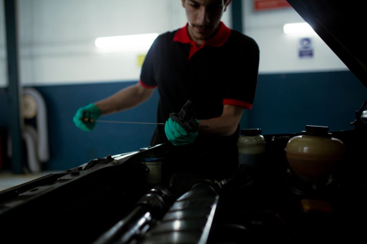 Mechanic under a raised hood wiping an engine oil dipstick with a cloth