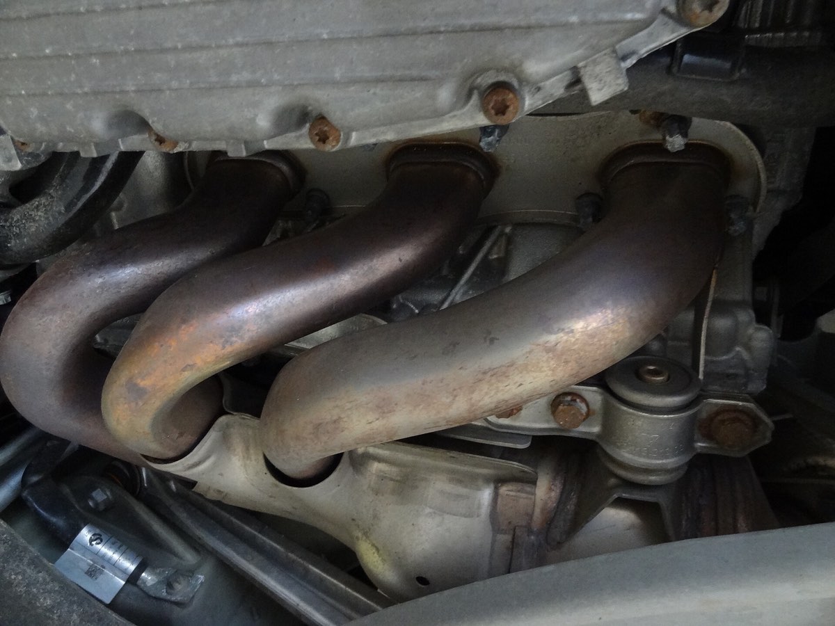 A four-branch exhaust manifold bolted to the side of a cylinder head, its tubes discolored from heat