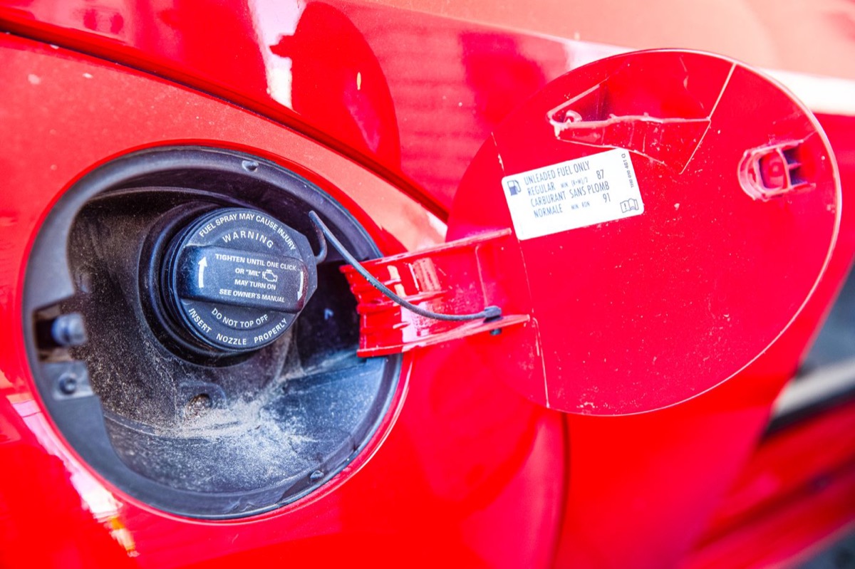 An open fuel filler door with the cap printed TIGHTEN UNTIL ONE CLICK OR MIL MAY TURN ON