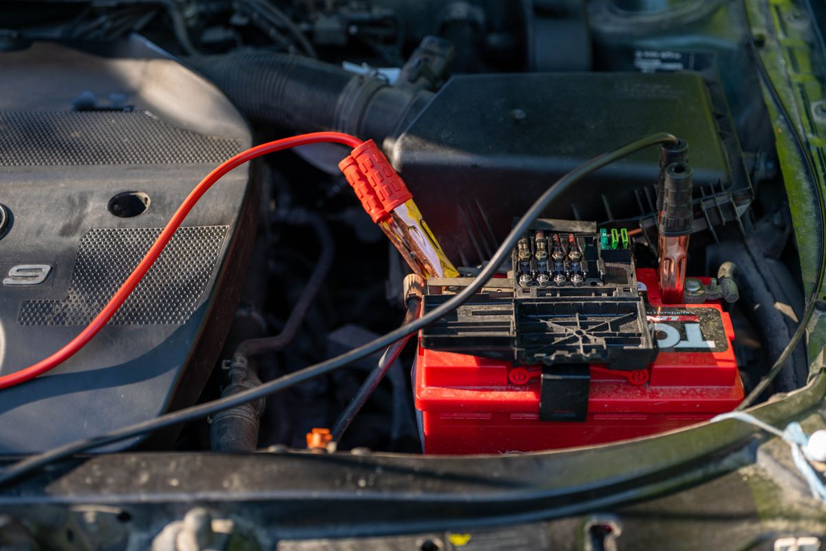 Jumper cable clamps attached to the terminals of a red car battery in an engine bay