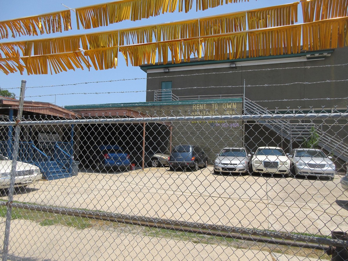 Rows of used cars parked close together on a small urban dealer lot