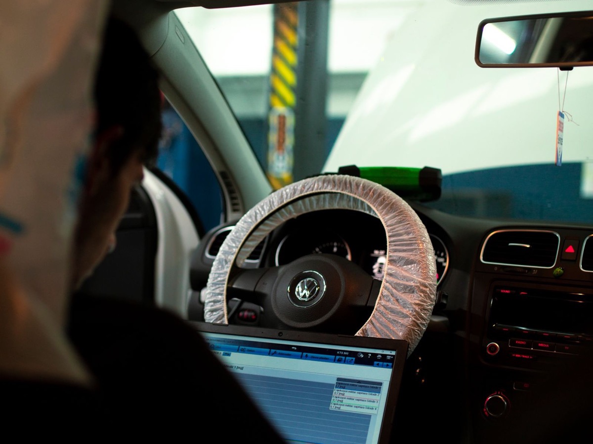 A technician in the driver's seat with a diagnostic laptop open, its screen listing a reading for each cylinder