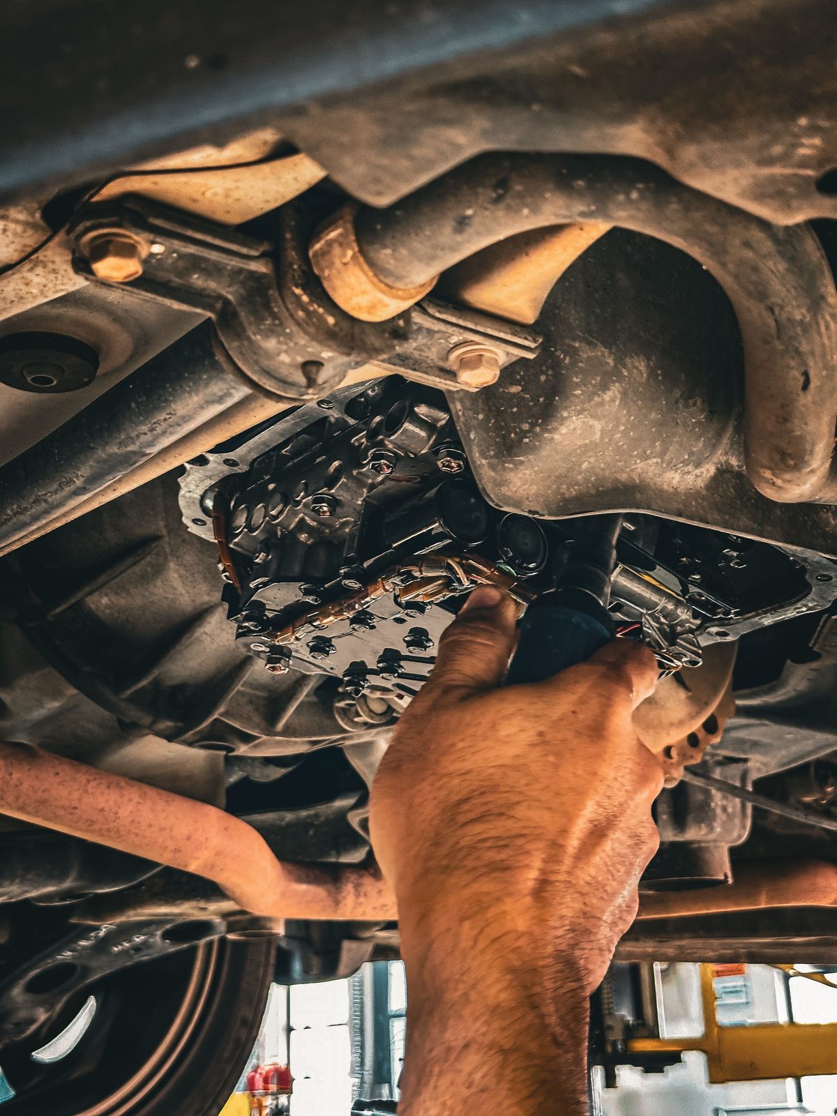 A mechanic working under a car on a lift with the automatic transmission pan removed, the filter and valve body exposed