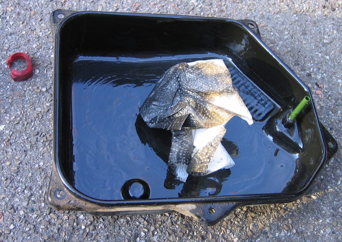 The dropped oil pan of an automatic transmission with dark settled sludge covering its floor